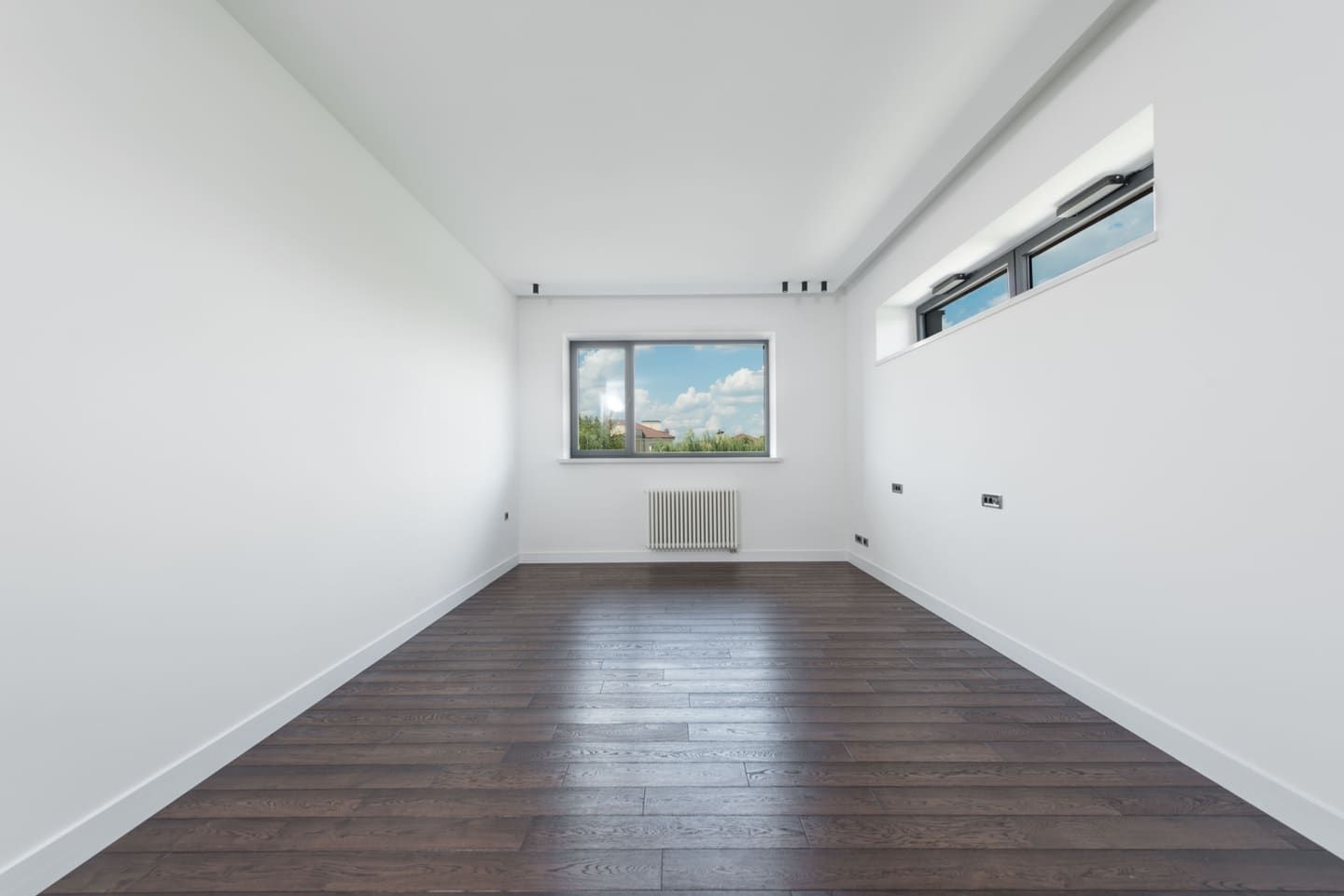 Leerer heller Wohnraum mit weißen Wänden, dunklem Parkett und einem Fenster